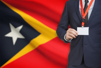 Businessman holding name card badge on a lanyard with a national flag on background - East Timor