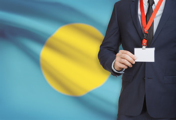 Businessman holding name card badge on a lanyard with a national flag on background - Palau