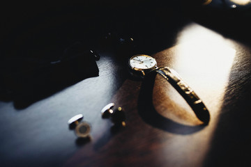 Man's cufflinks and wristwatch lying on a wooden table