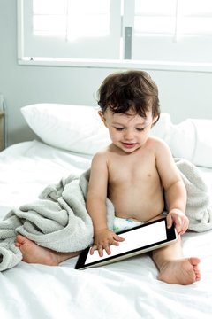 Cute baby boy using tablet PC on bed