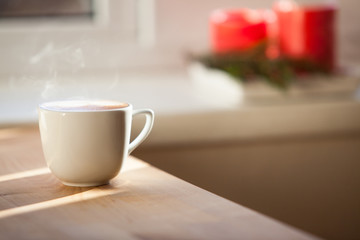 A cup of coffee on table and red blurred candles on background

