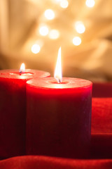 Lit red candles , on red wavy fabric and golden background with bokeh.