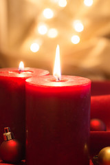 Lit red candles with Christmas balls , on red wavy fabric and golden background with bokeh.