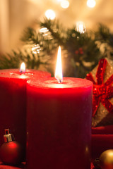 Lit red candles with Christmas balls , on red fabric and golden background with bokeh.
