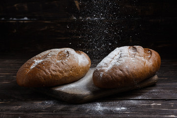 Two black bread with flour on a wooden background. Advertising bread. Leaning flour.