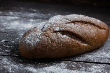 One black bread with flour on a wooden background. Advertising bread. Leaning flour.