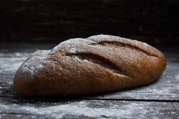One black bread with flour on a wooden background. Advertising bread. Leaning flour.
