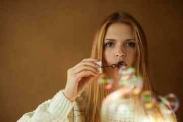 Fashionable model with long red hair blows soap bubbles