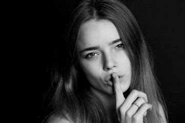 Naklejka premium The girl with long hair holds finger near the lips . The gesture of silence, secrecy, secret