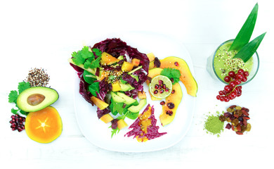 Buntes Superfood als Salat auf Teller und grüner Smoothie auf weißem Holz-Hintergrund