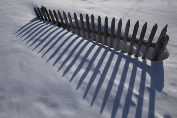 A fragment of a wooden fence and shadow on the snow. Yakutia. Russia.