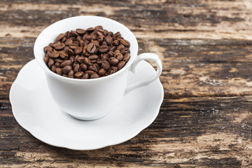 Coffee beans in white cup on wooden table.