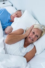 Senior woman covering ears while man snoring