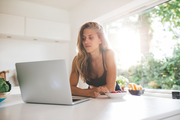 Beautiful female in kitchen using laptop