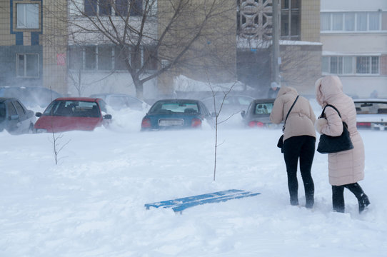 Pedestrians Make Their Way Through The Blizzard In The City Against The Backdrop Of Snow-covered Cars And Houses.