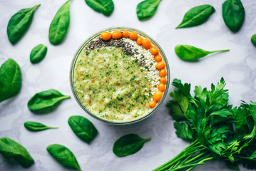 green smoothie with sea buckthorn, Chia seeds and sesame seeds on a white table, around spinach leaves and a bunch of parsley. The concept of healthy eating, vegetarian and vegan food, top view