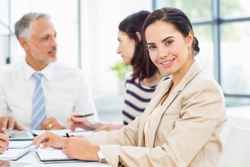 Businesswoman smiling at camera while colleagues discussing