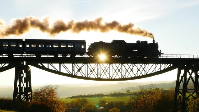 romantic scenery of steam engine locomotive crossing bridge at sunset sky.