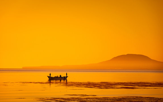 Silhouette in the golden sunrise of bait fishing boat panga off Loreto on the Sea of Cortez with Coronado Island on the horizon