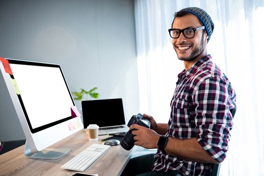 Attractive hipster smiling at camera while working at desk