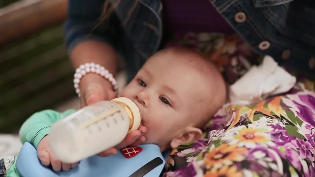 Mother feeds baby from a bottle in his lap. Close-up.
