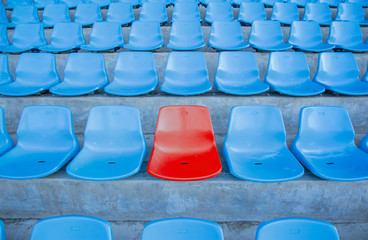 Single or one red seat or bench in the middle or center of blue chair in the football or soccer stadium.