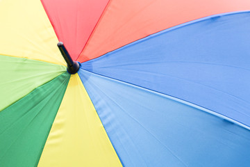 Nahaufnahme eines geöffneten grossen Regenschirms mit schwarzer Spitze und Regenbogenfarben