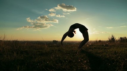 Silhouette of sporty woman practicing yoga in the park at sunset - drop back, wheel pose. Sunset light, sun lens flares, golden hour. Freedom, health and yoga concept