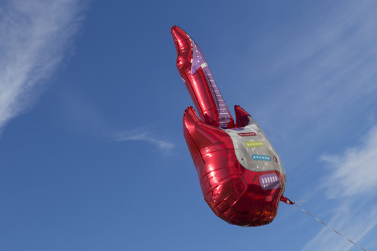 Ein roter Luftballon in Form einer elektrischen Gitarre schwebt im blauen Himmel.