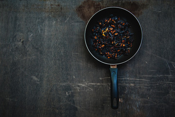 The failure on kitchen: burnt charred vegetables in frying pan on dark shabby background