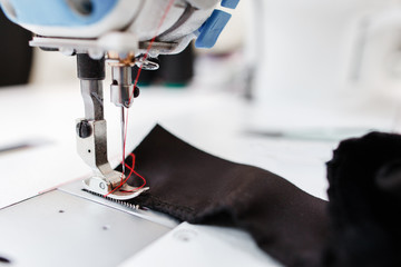 Sewing machine stitching dark fabric close-up. Detail photo of shuttle of needle working process. Garment industry, seamstress workplace, tailor workshop concept