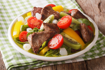 salad of roast beef, kiwi fruit, tomatoes, peppers and arugula close-up in a bowl. Horizontal