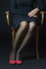 Woman in red pumps and black stockings is sitting with parallel legs on an old chair. This position reflects smartness, confidence, creditibility.
