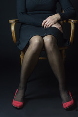 Woman in red pumps and black stockings is sitting with parallel legs on an old chair. This position reflects  
openness, cool and ease bordering on naivete.