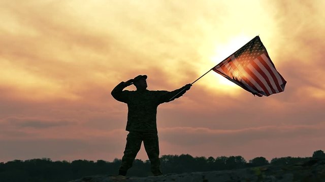 
Soldier  salute American flag  against gloomy orange  sky. Slow Motion
