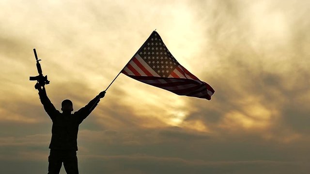 Soldier stand with American flag and rifle against gloomy orange  sky. Slow Motion