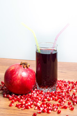 A glass of delicious pomegranate juice, pomegranate and pomegranate seeds on a table