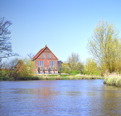 Fototapeta na wymiar Idyllic river scene with old house and blue sky, spring scene.