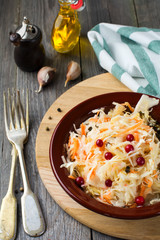 Sour cabbage with cranberries in a ceramic plate on old wooden background. Rustic style. Selective focus.
