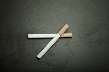Two cigarettes on a black slate cutting board. Toned