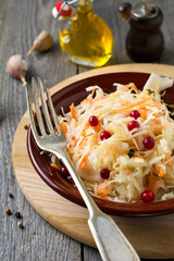 Sour cabbage with cranberries in a ceramic plate on old wooden background. Rustic style. Selective focus.