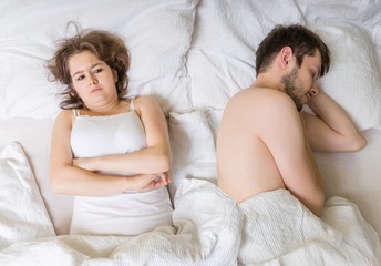 Impotence concept. Young man is sleeping in bed. Sad, disappointed and unsatisfied girlfriend lying near.