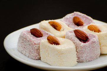 Turkish Delight with almonds on a saucer, close-up, black background