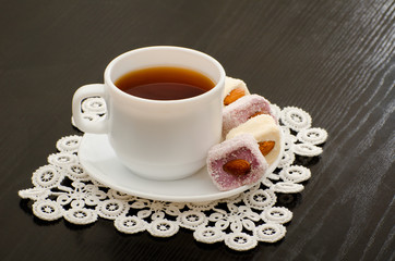 Mug of tea and Turkish delight with nuts on a plate, close-up, black background