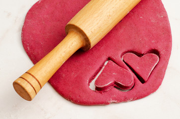 Red beet dough with two cut hearts out and rolling pin on a white table