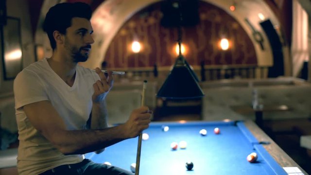 Happy man sitting on billiard's table and talking on loudspeaker
