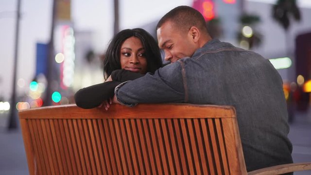Happy Black couple sitting on public bench on city street looking in to each others eyes