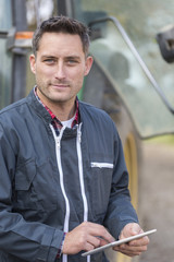 Farmer leaning on the tractor using a digital tablet
