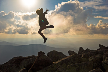 Hiker with backpack jumping over rocks  sunset sky on the background