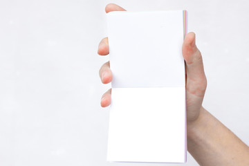 Hand holds notebook open. Blank white paper. Place for an inscription